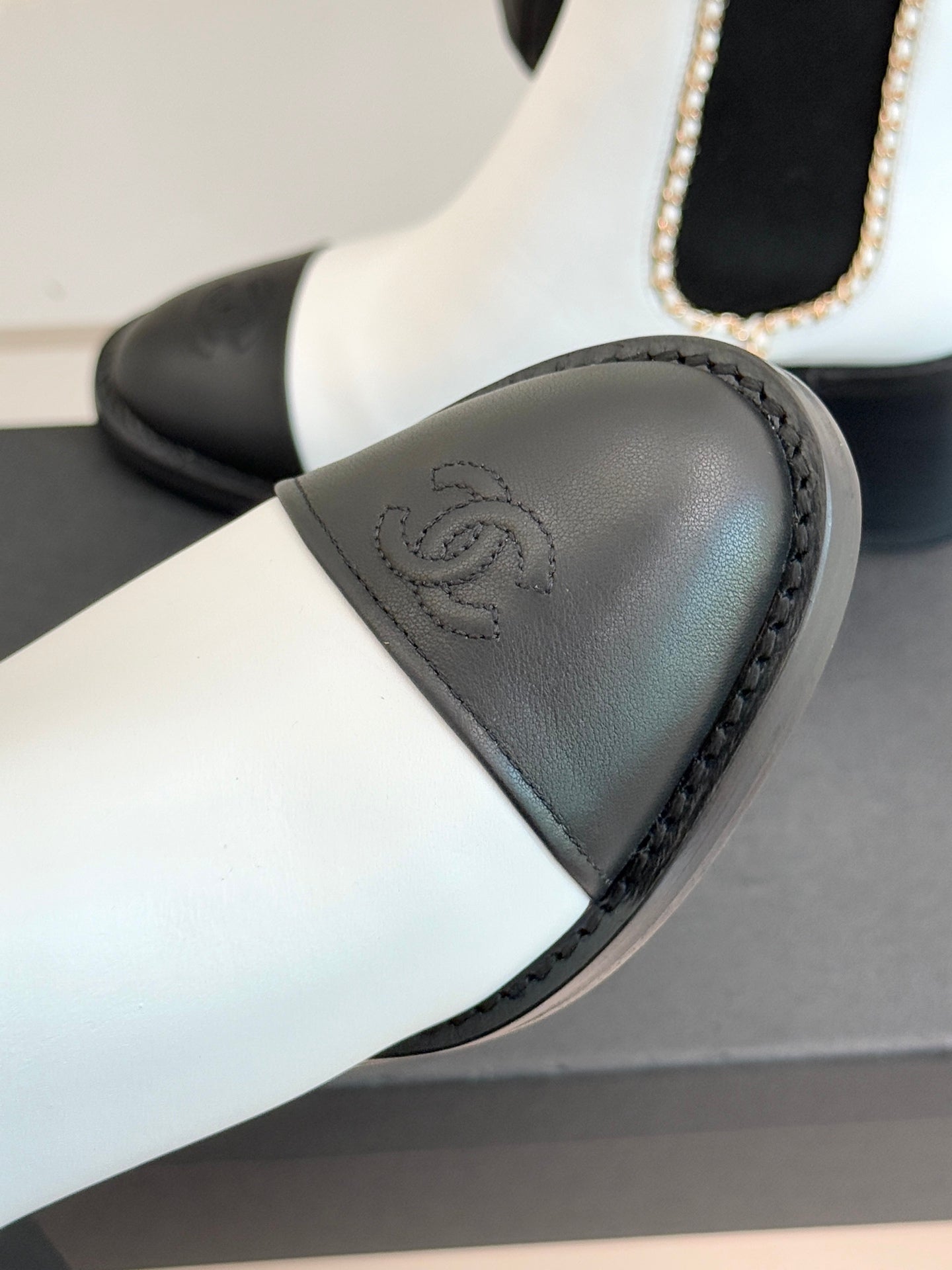 White and black Chelsea boot detail showing black toe cap and embossed logo.