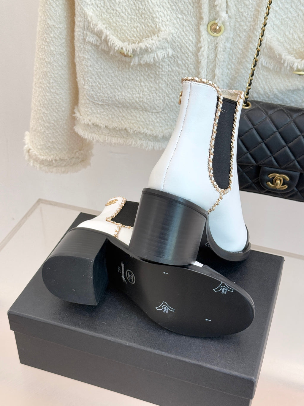 White Chelsea boots on a black box showing gold-trimmed elastic side panels and heel.