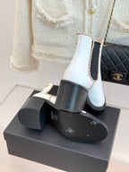 White Chelsea boots on a black box showing gold-trimmed elastic side panels and heel.