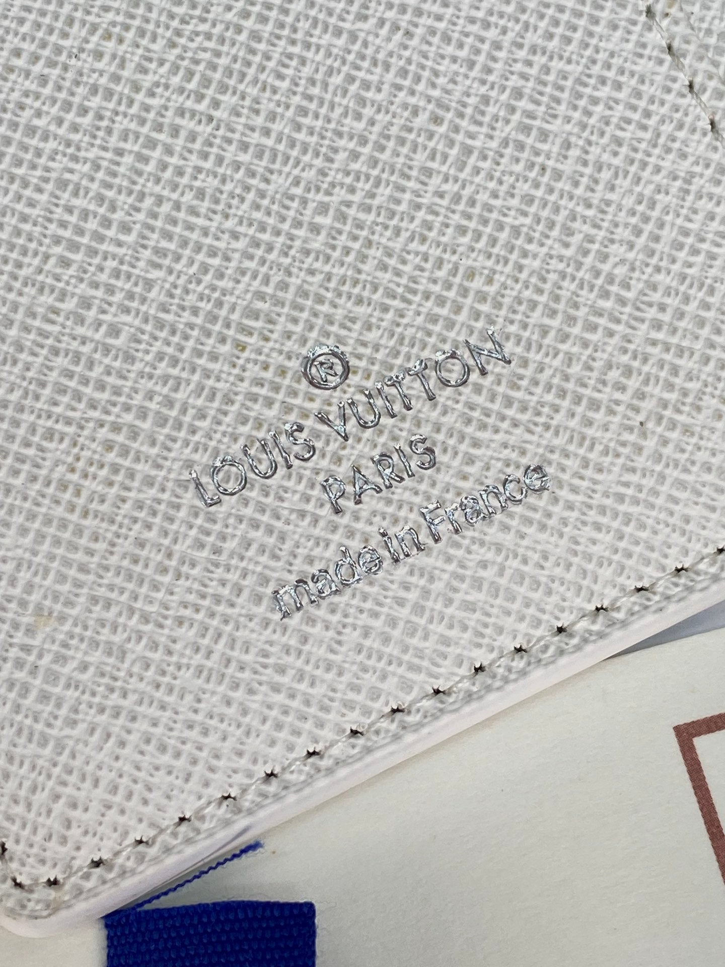 Small bag close-up of light textured material with stitched edge and embossed logo.
