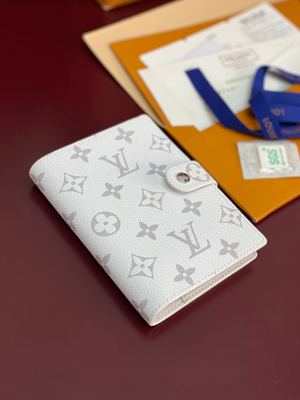 Small bag in light color with embossed monogram pattern and metal snap closure.