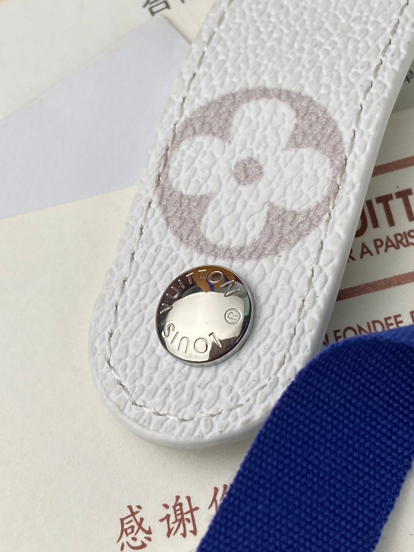 Small bag close-up: white textured leather with round clasp and monogram patch, pink tint.