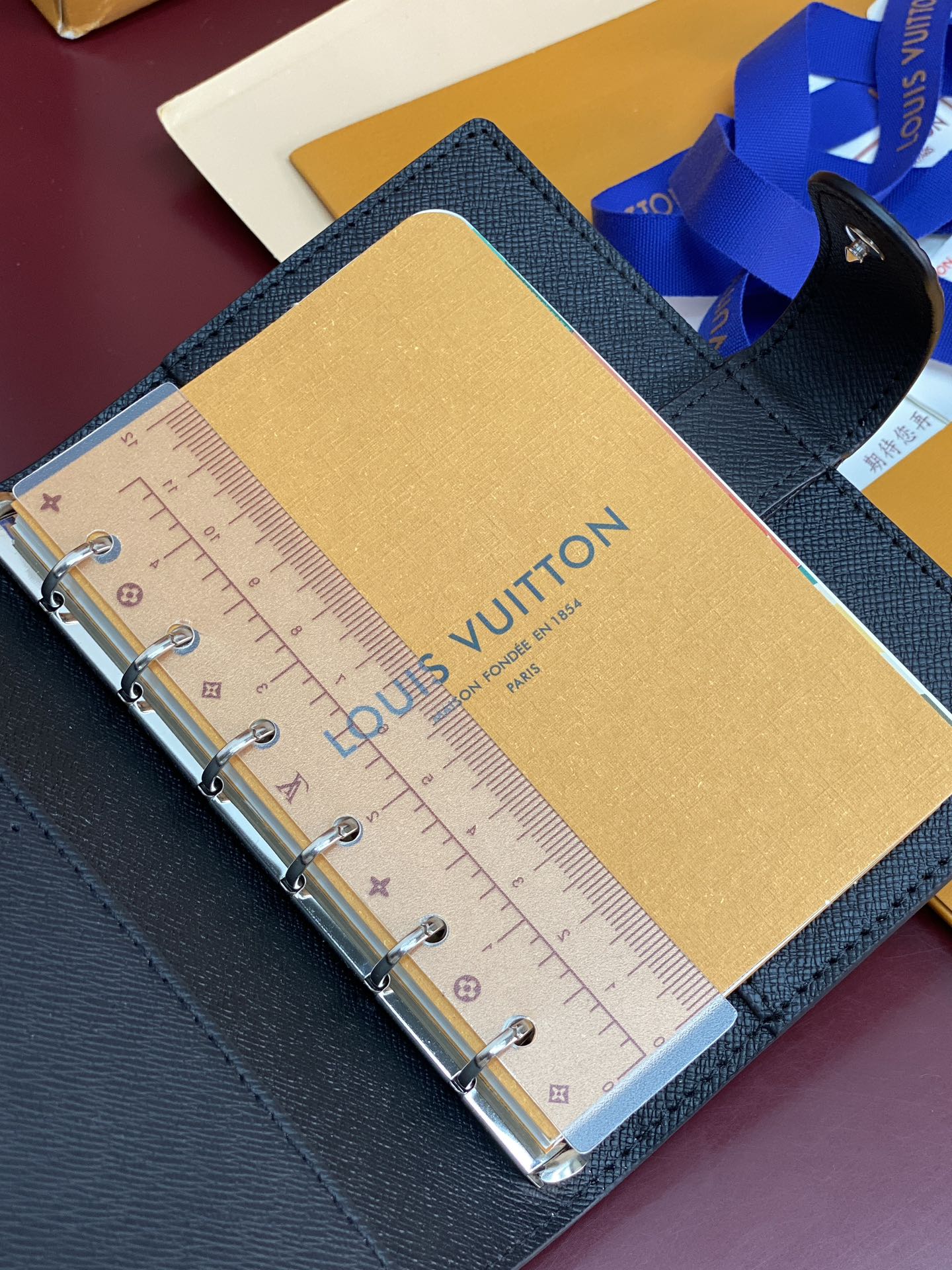 Louis Vuitton small bag open, showing ruler-style planner card on tan interior panel.