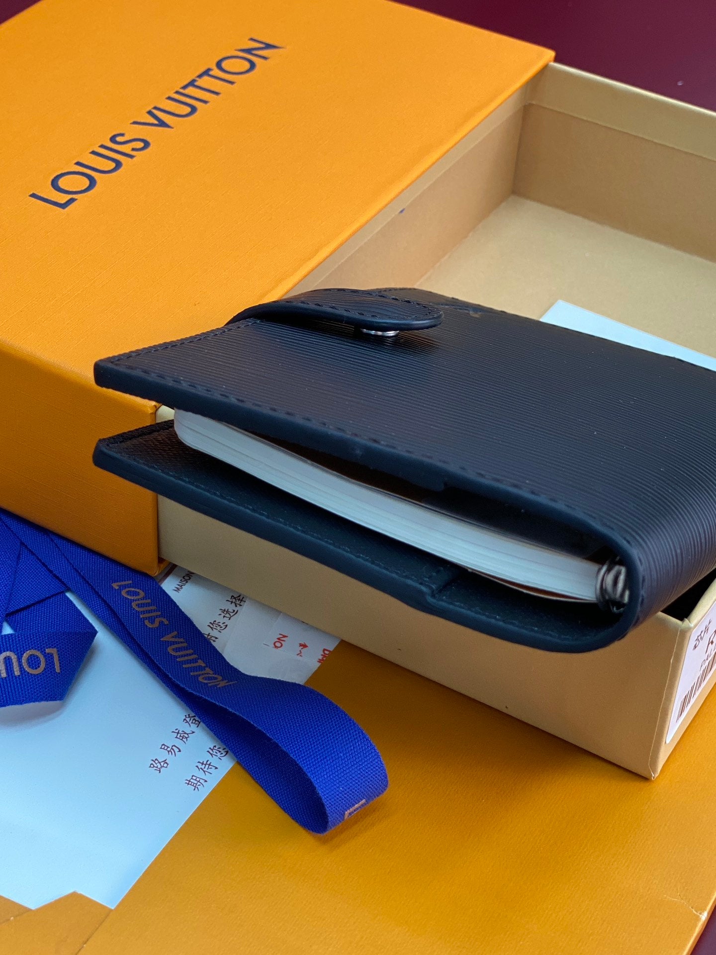 Small bag with dark navy foldover flap and snap button, shown in a box