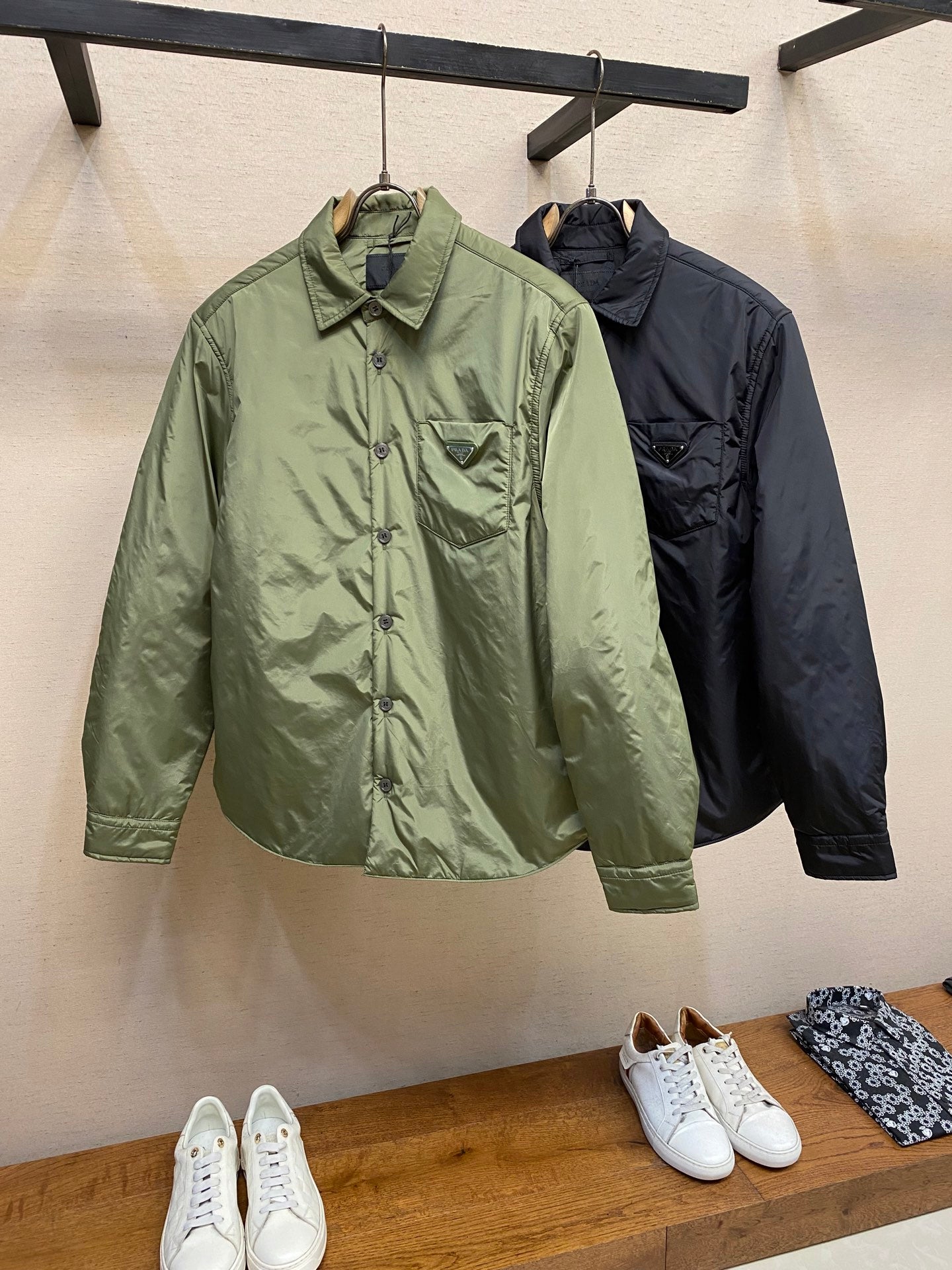Green and dark Prada long-sleeve jackets hanging side by side, button front and collar