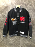 Black varsity jacket with striped rib collar, front snaps, and colorful logo patches