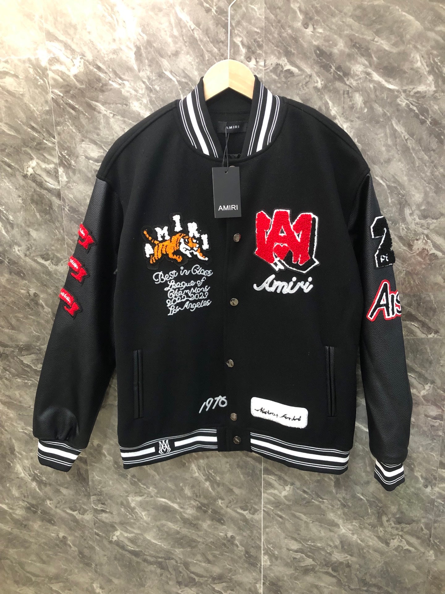 Black varsity jacket with striped rib collar, front snaps, and colorful logo patches