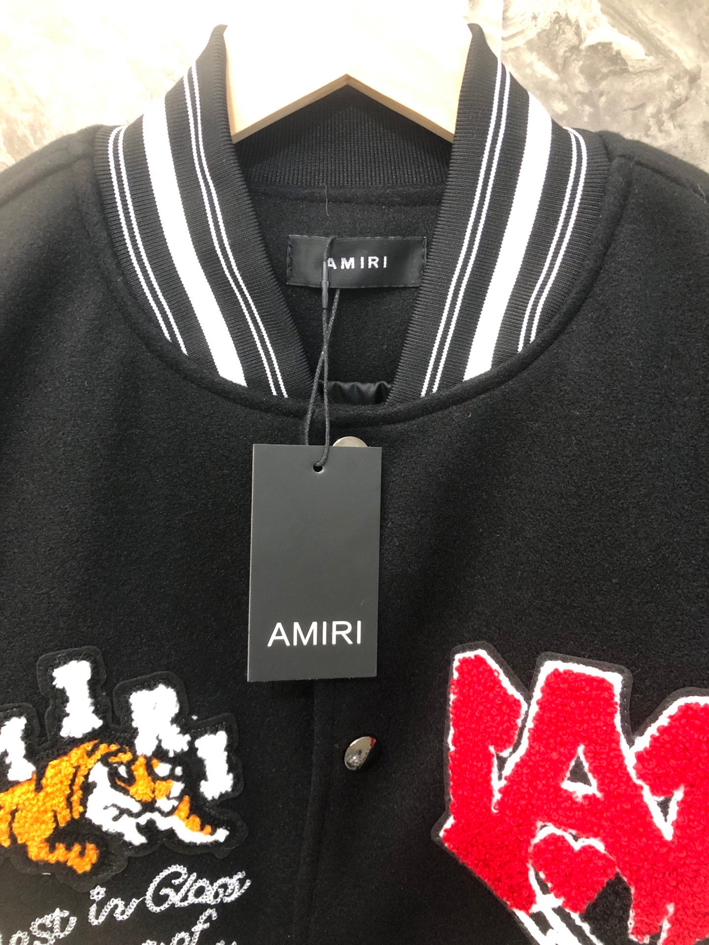 Black knit varsity collar with hanging AMIRI tag and embroidered front patches