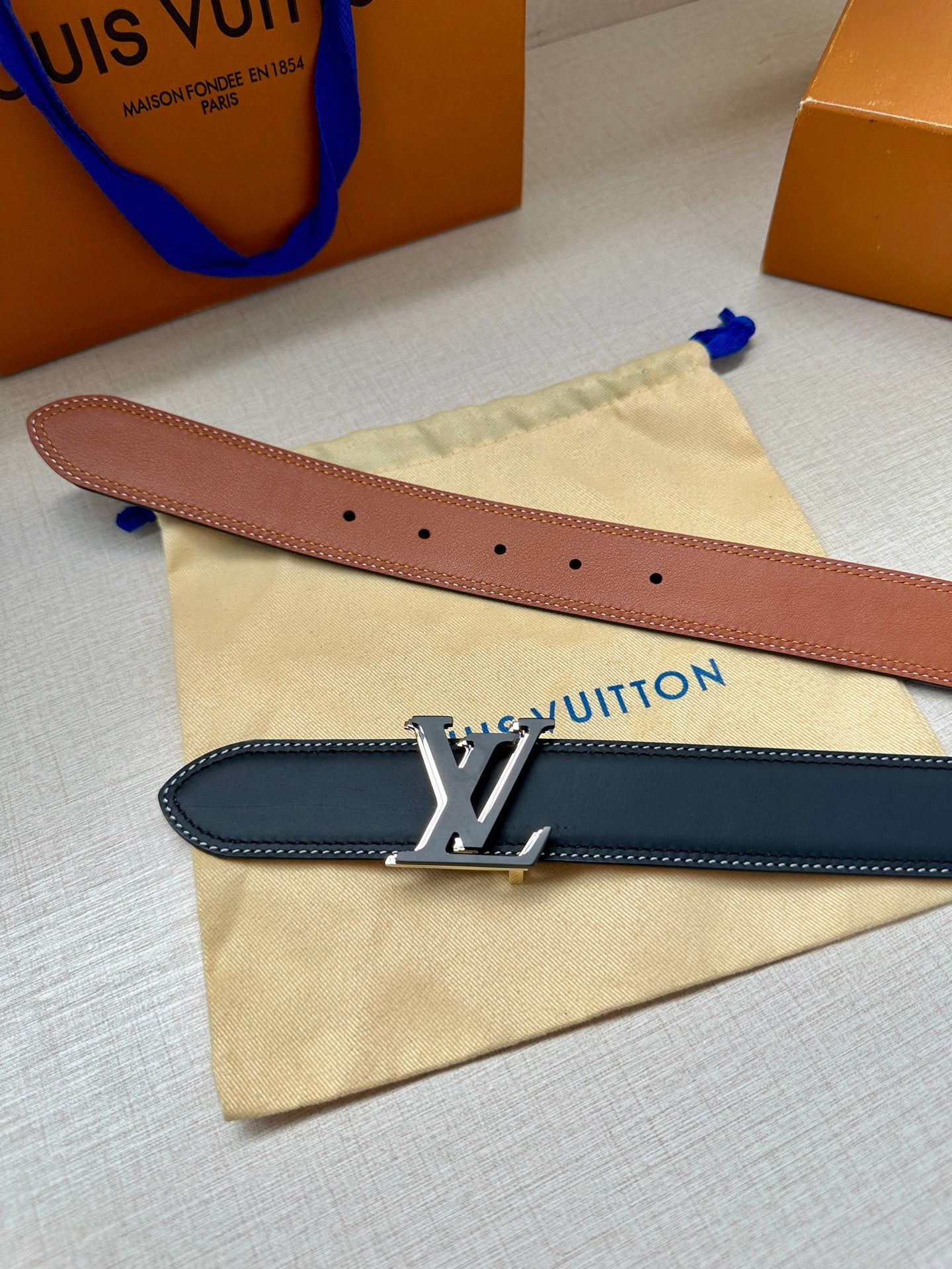 Louis Vuitton belts, tan and dark navy leather straps with silver-toned buckle.