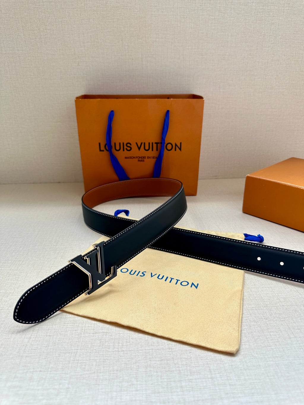 Louis Vuitton leather belt, dark navy with gold LV buckle and rows of adjustment holes.