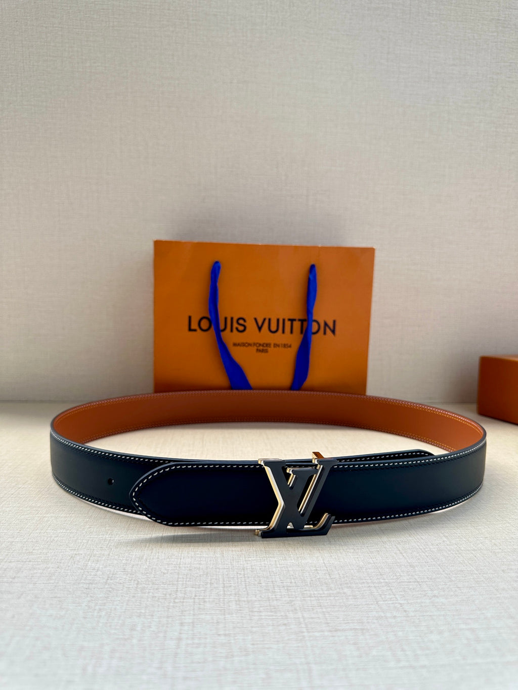 Louis Vuitton leather belt, dark navy with gold LV buckle and stitched edges.
