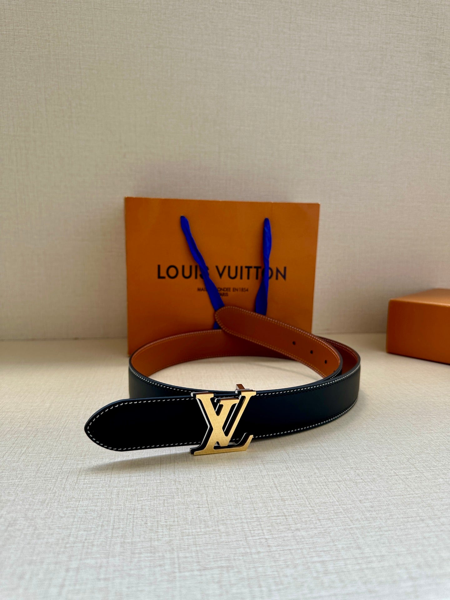 Navy leather belt with gold-tone LV buckle and brown strap, side view
