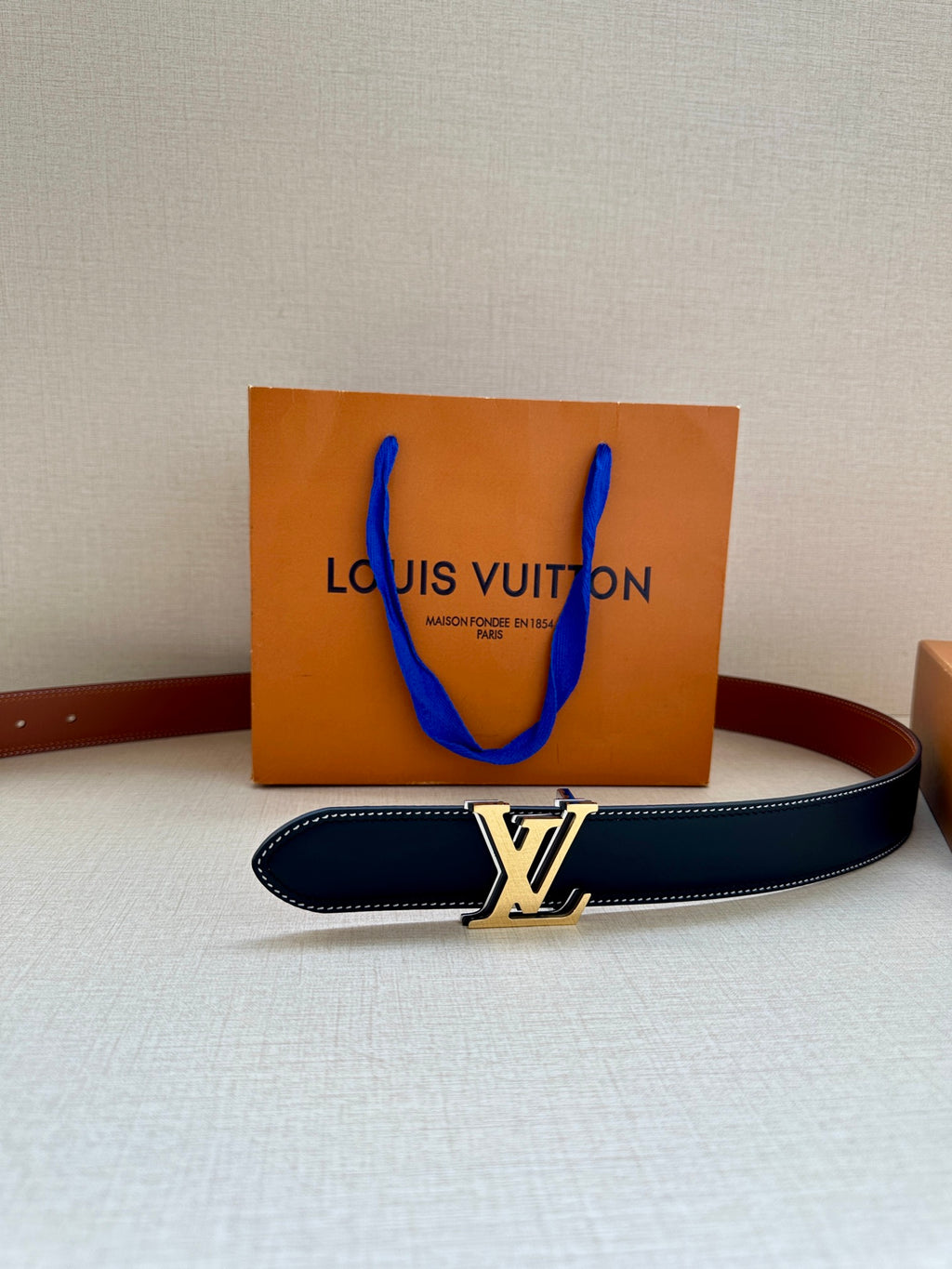 Navy leather belt with gold-tone LV buckle and tan edge stitching, flat view