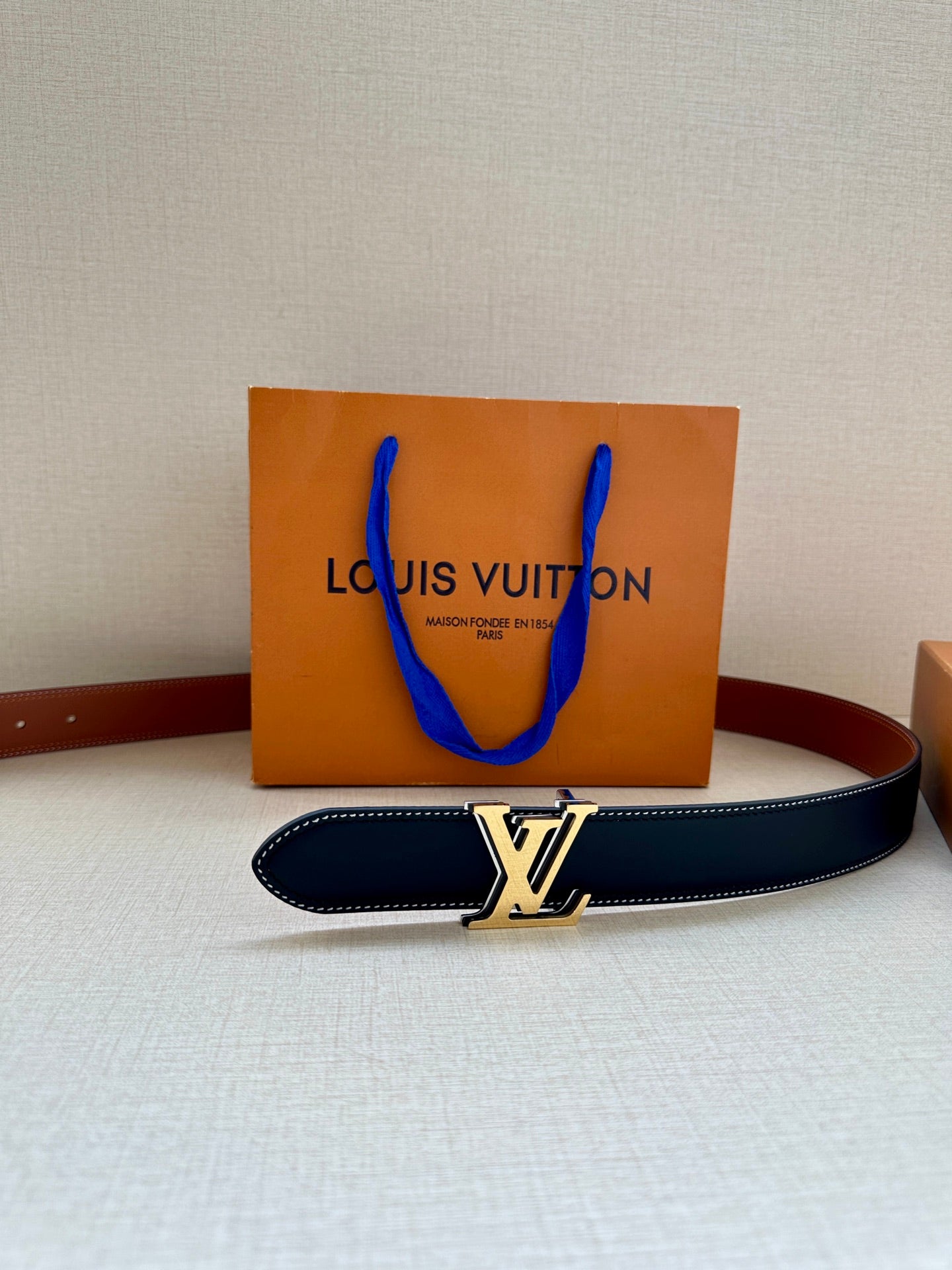 Navy leather belt with gold-tone LV buckle and tan edge stitching, flat view