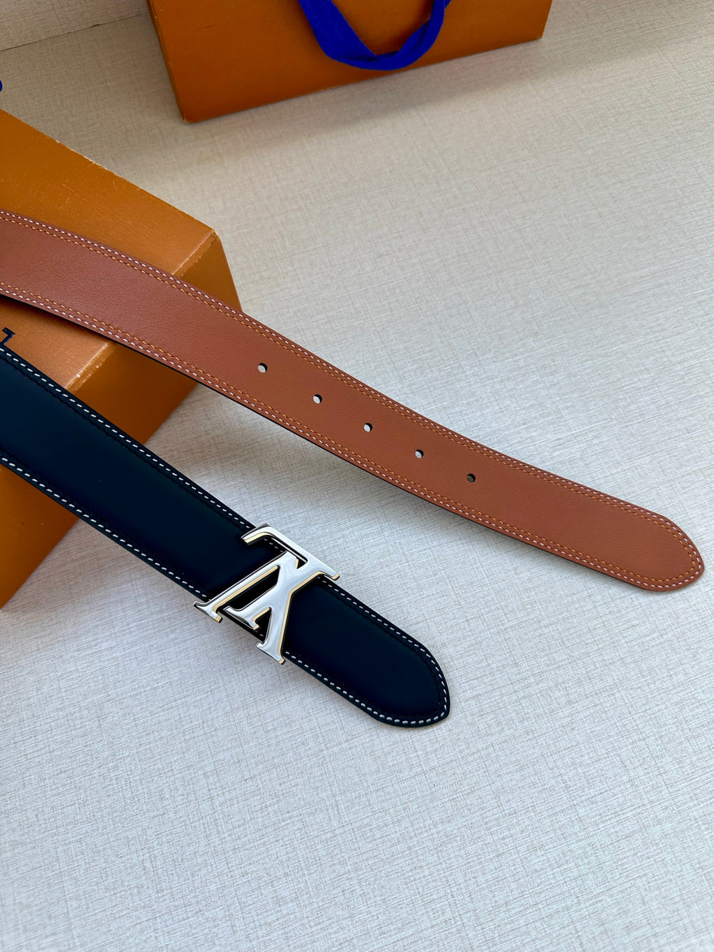 Leather belt with navy strap and gold LV buckle, plus a tan strap option