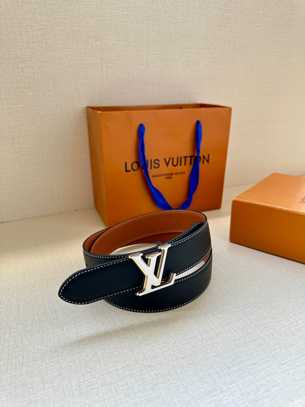Leather belt with navy strap and gold LV buckle with tan lining visible
