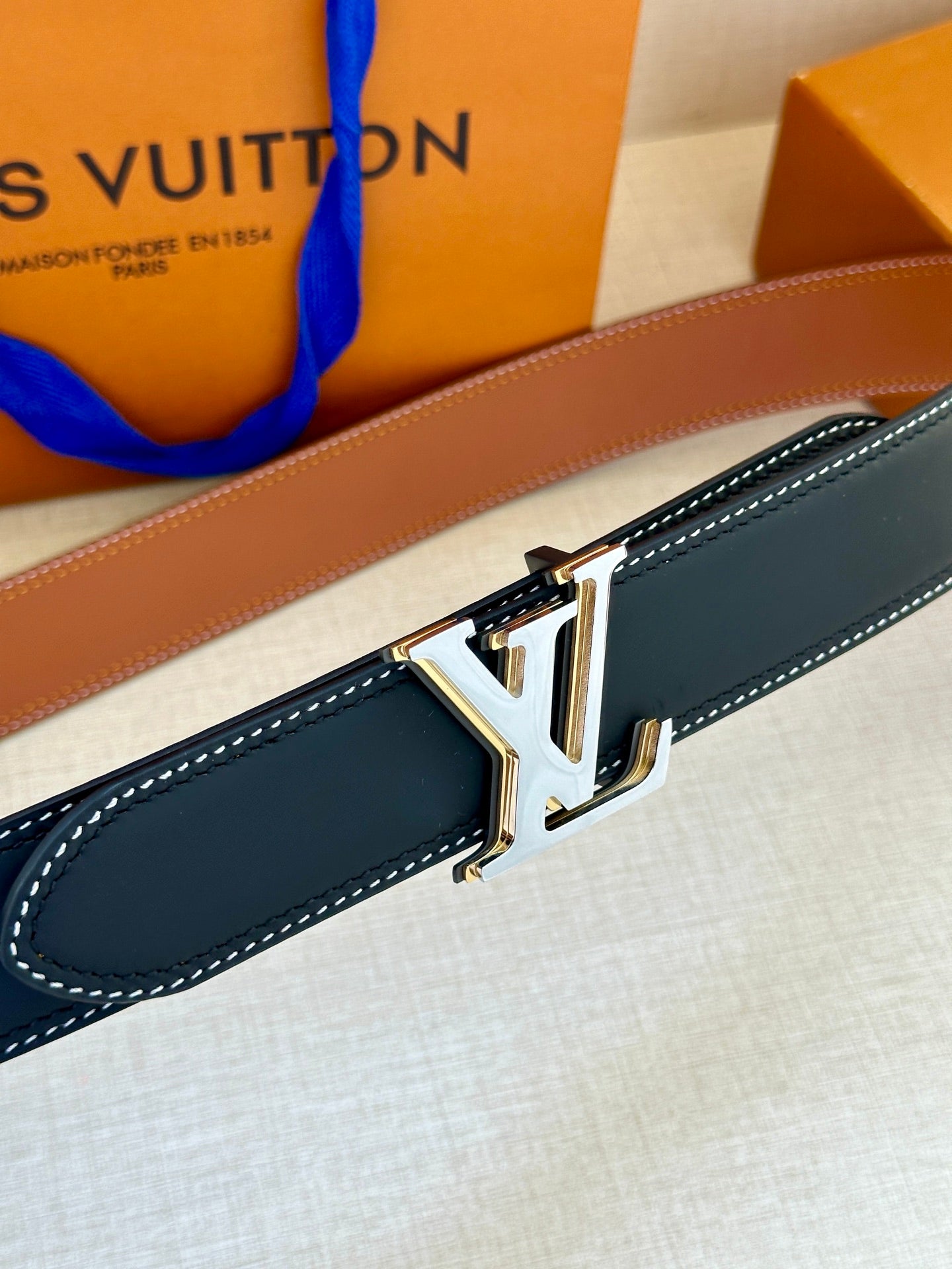 Leather belt close-up with navy strap, white stitching, and gold LV buckle