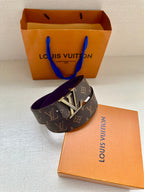 Louis Vuitton belt with dark monogram strap and gold LV buckle, laid across box.
