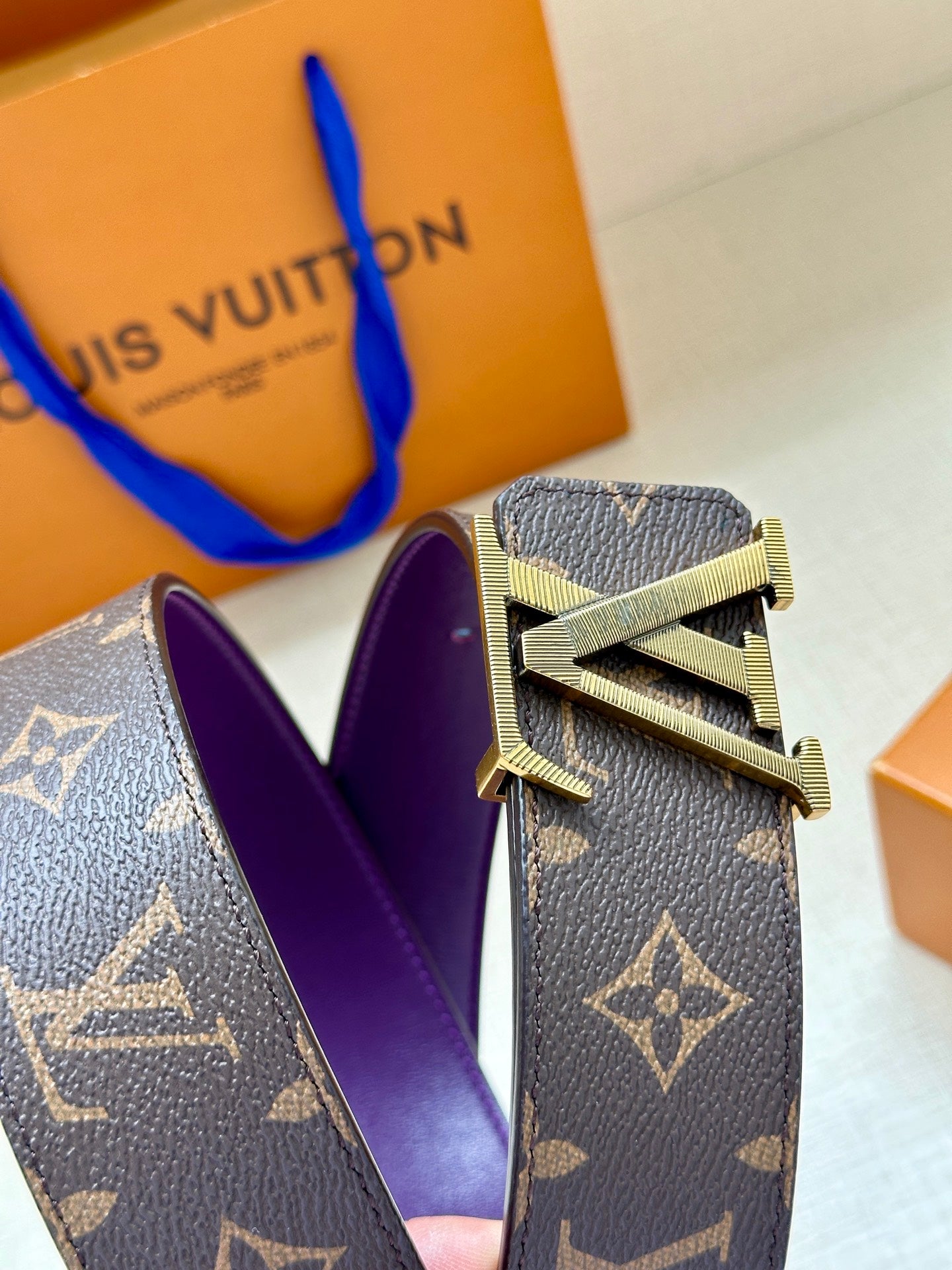 Louis Vuitton belt buckle detail on dark monogram strap with purple lining.