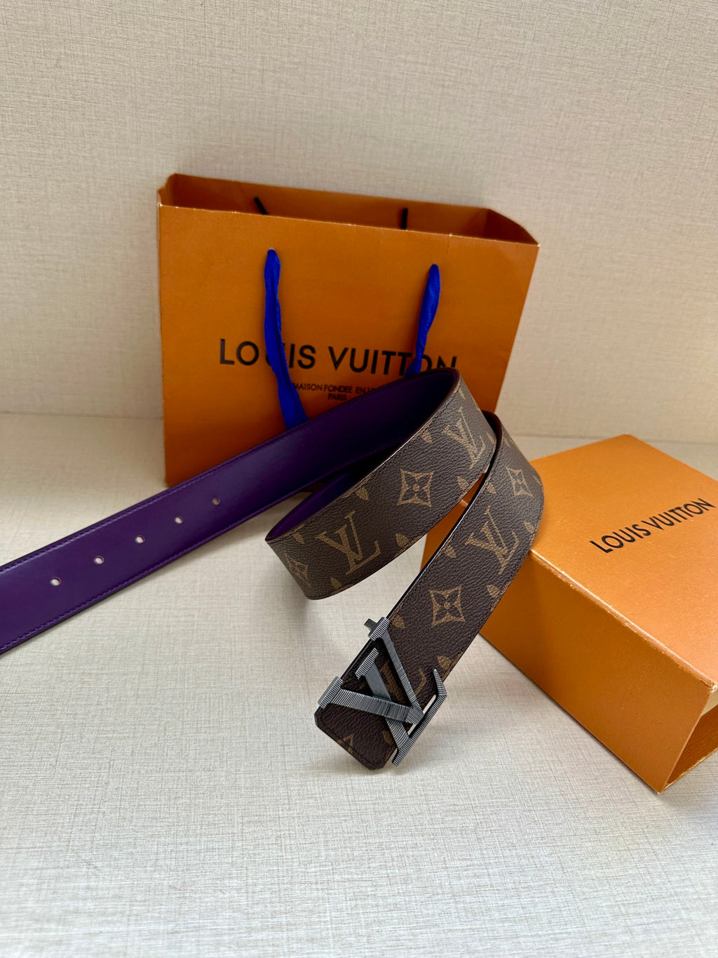 Louis Vuitton belt angled view, dark monogram strap with purple underside and gold buckle.