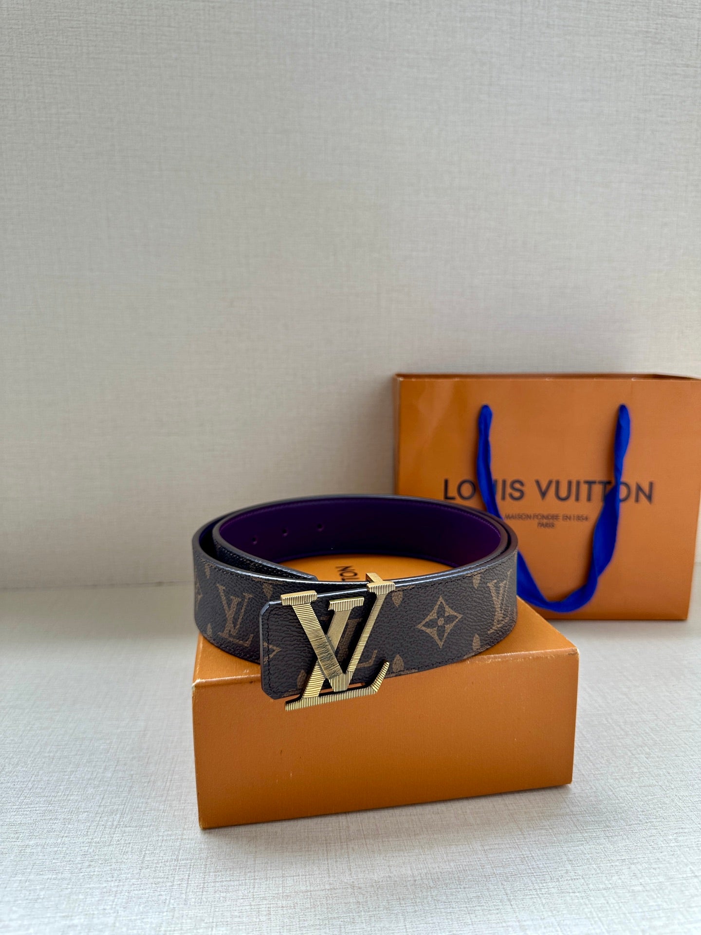 Louis Vuitton belt side view, dark monogram strap and gold LV buckle with purple edge.