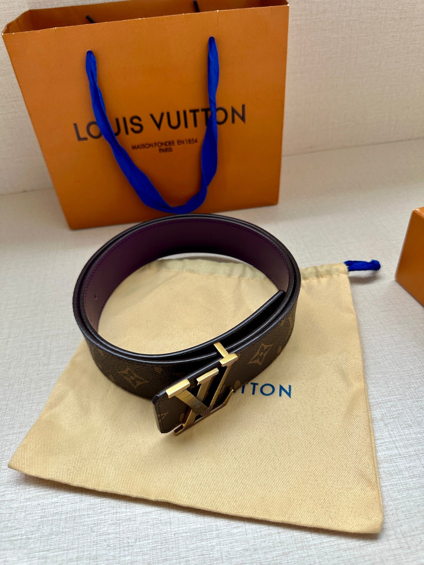 Louis Vuitton belt with dark monogram strap and gold LV buckle, purple lining.