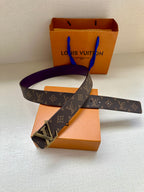 Louis Vuitton belt laid flat, dark monogram strap with gold LV buckle and purple underside.
