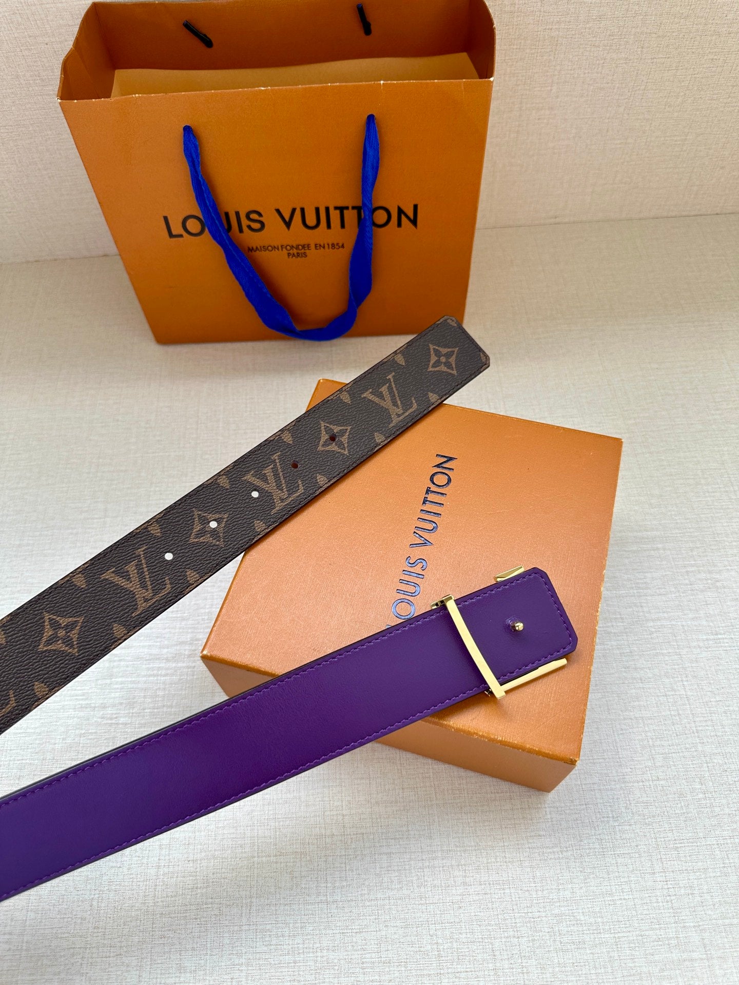 Monogram belt with purple strap and gold buckle, laid diagonally