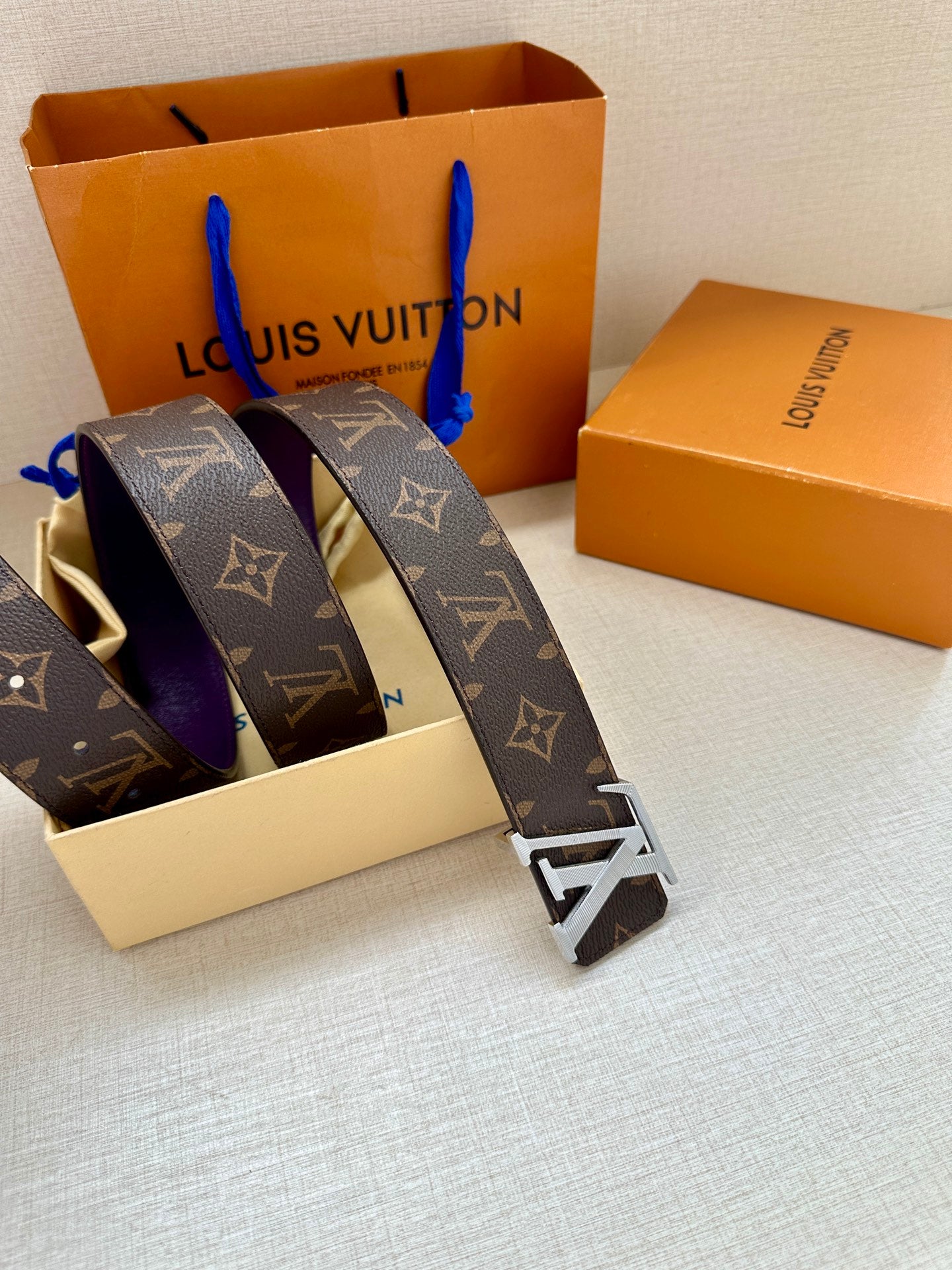 Monogram belt with purple strap and metal buckle, partially unboxed