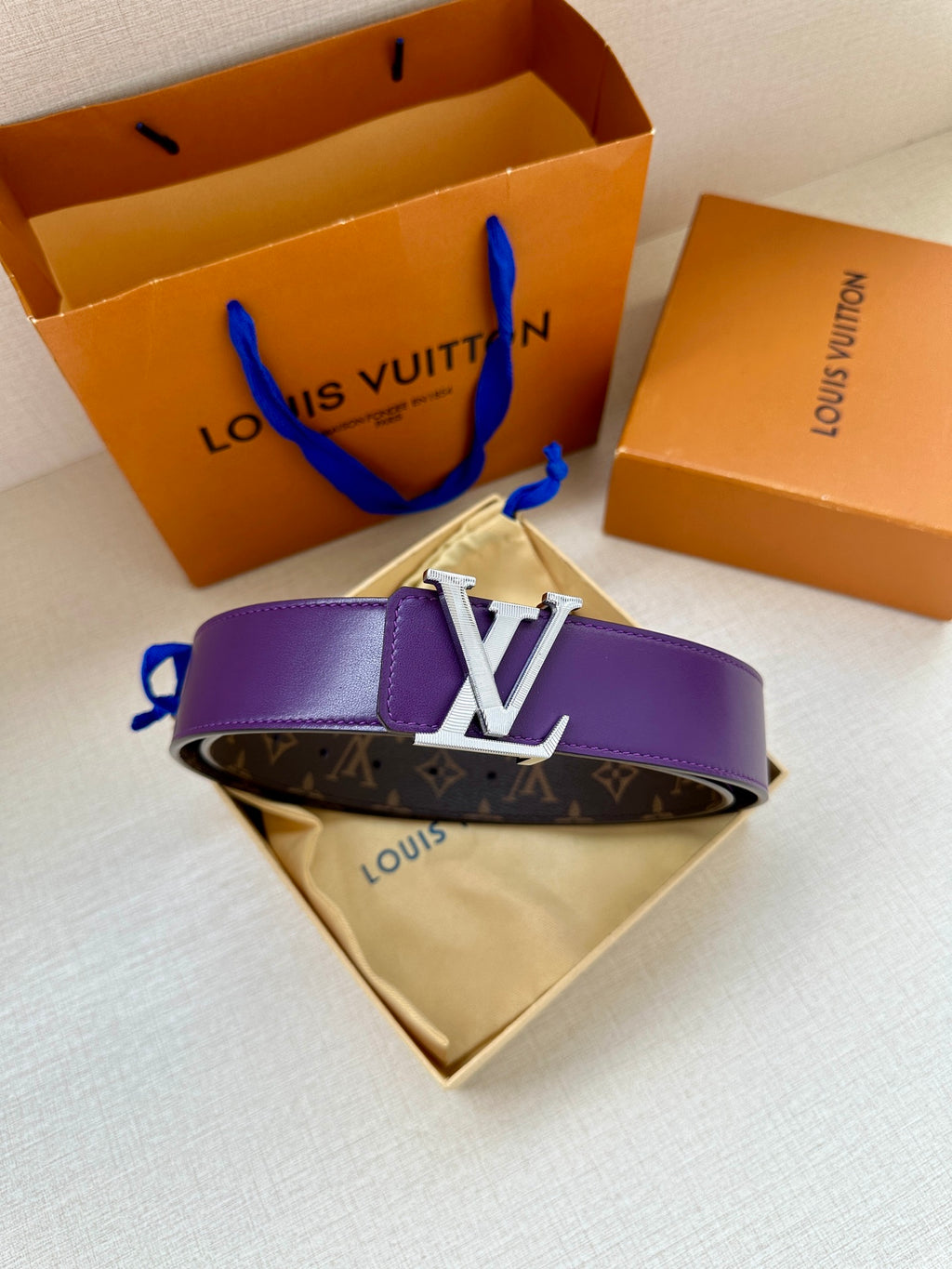 Monogram belt with purple strap and gold LV buckle, resting on folded cloth