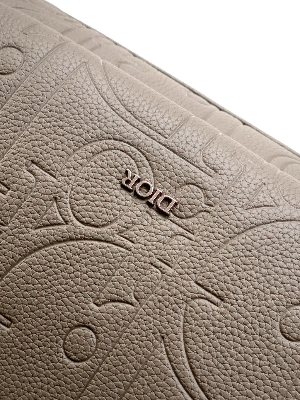 Dior mini backpack in light gray with embossed “DIOR” logo on textured leather
