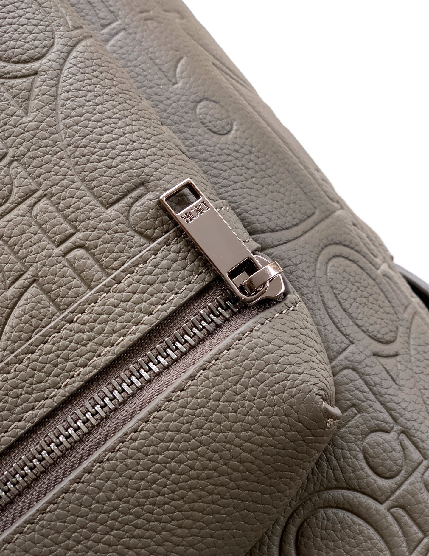 Light gray Dior men's backpack zipper pull on embossed leather panel close-up