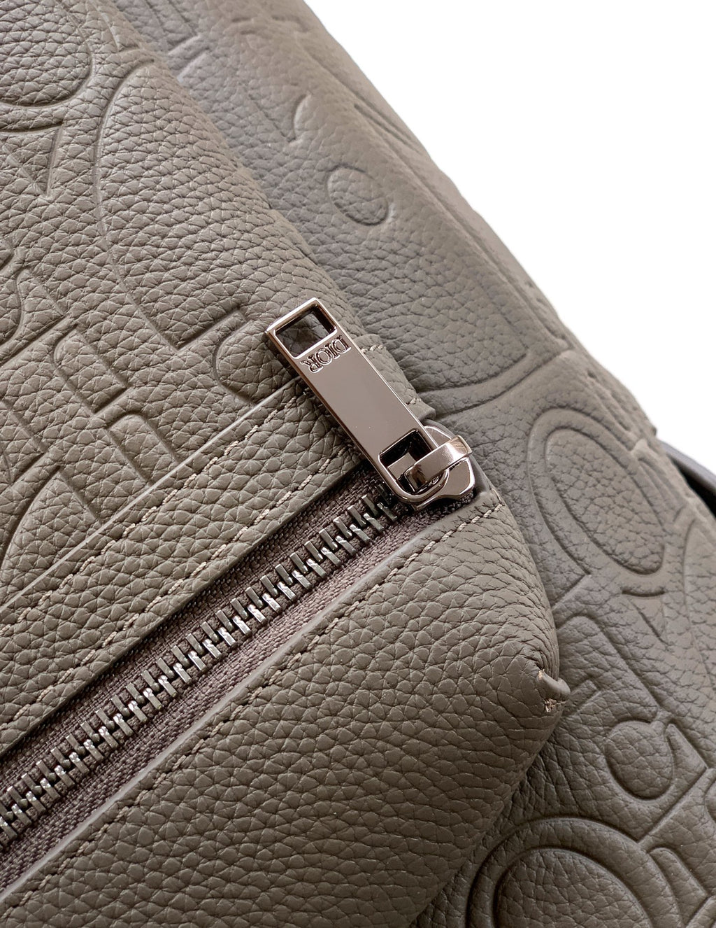 Dior mini backpack close-up of zipper pull and embossed leather texture