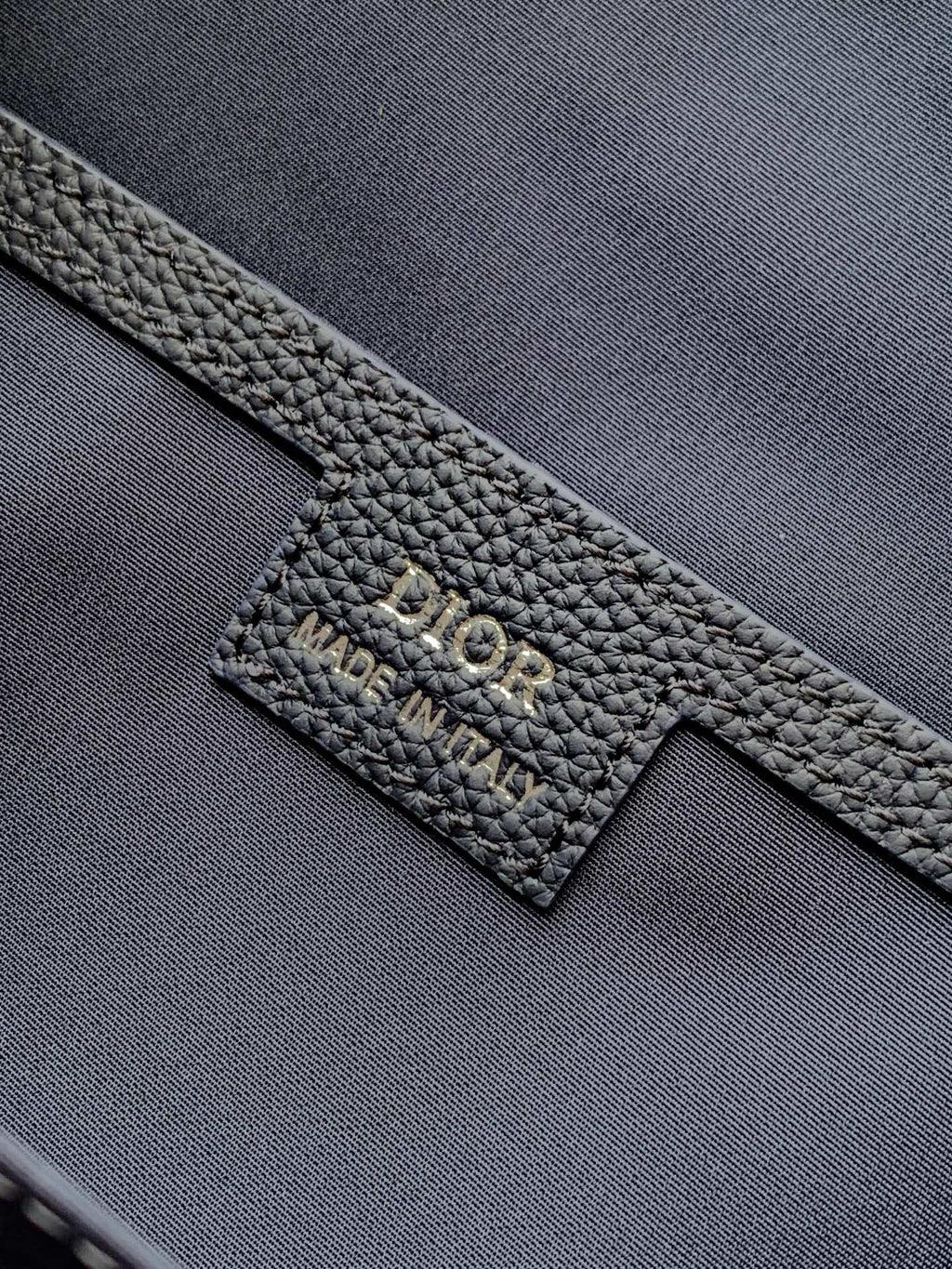 Dior leather logo patch on dark blue bag strap with embossed branding