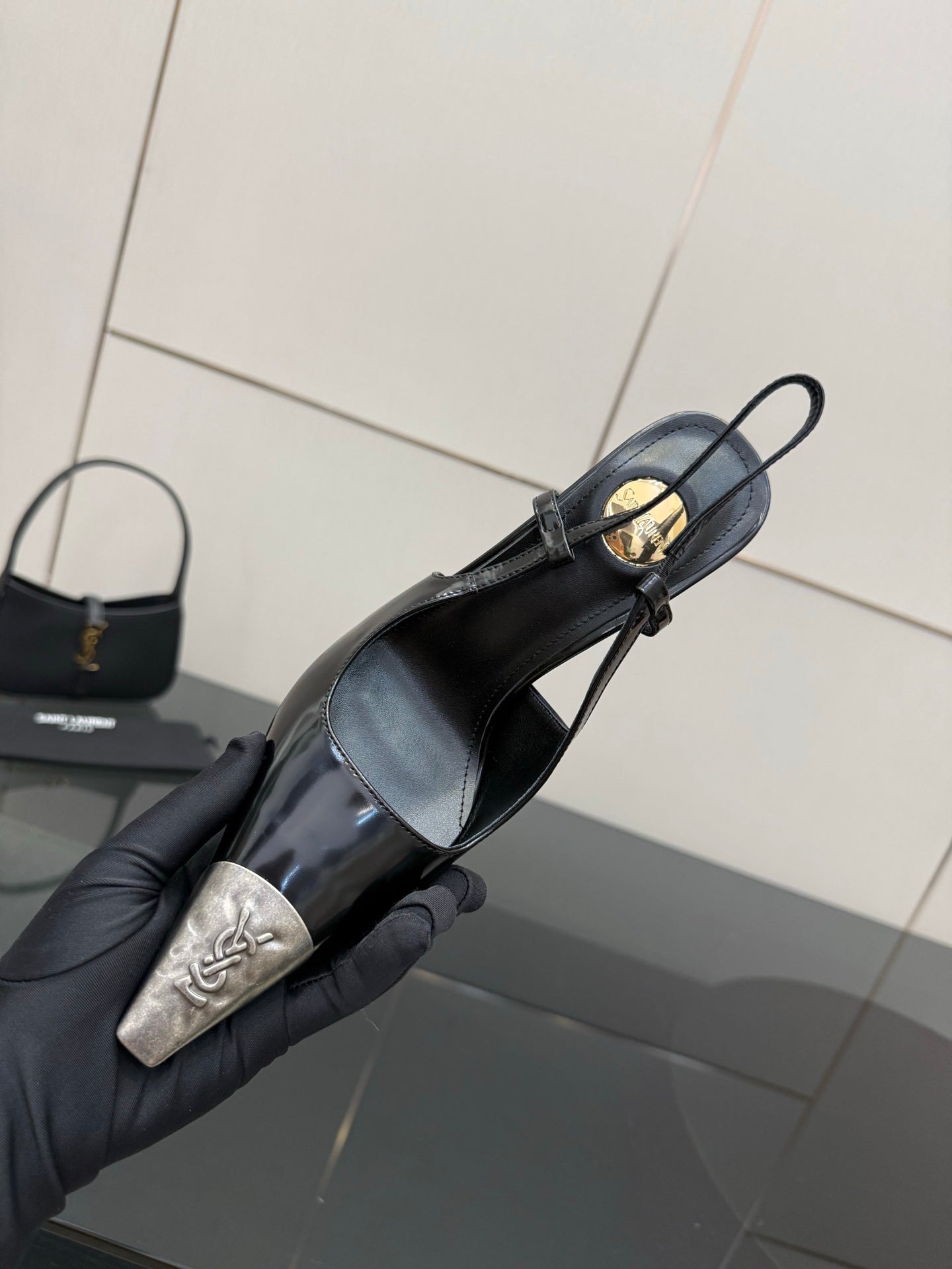 Women's YSL black pointed slingback pump with gold hardware, held in glove