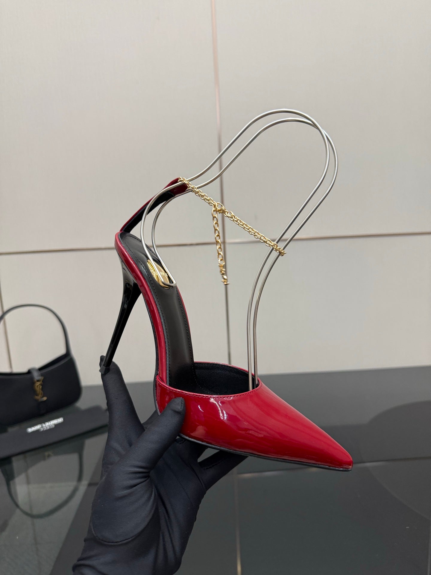 Women’s red patent pointed-toe stiletto heel with gold chain sling strap in hand
