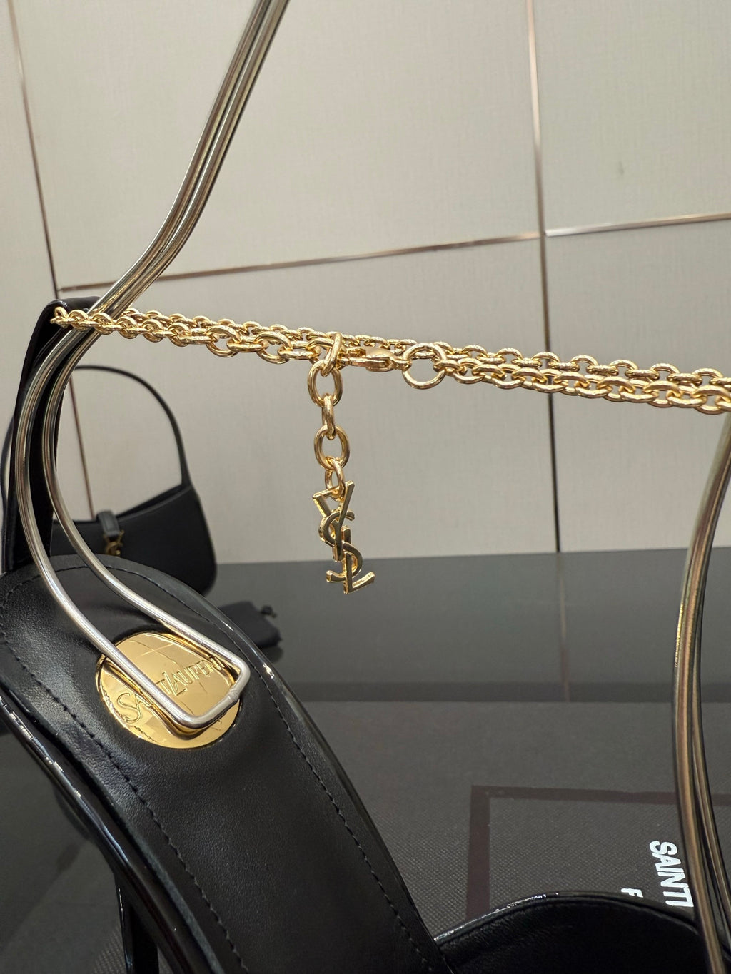 Black patent leather high-heel pump with gold chain strap and logo heel inlay