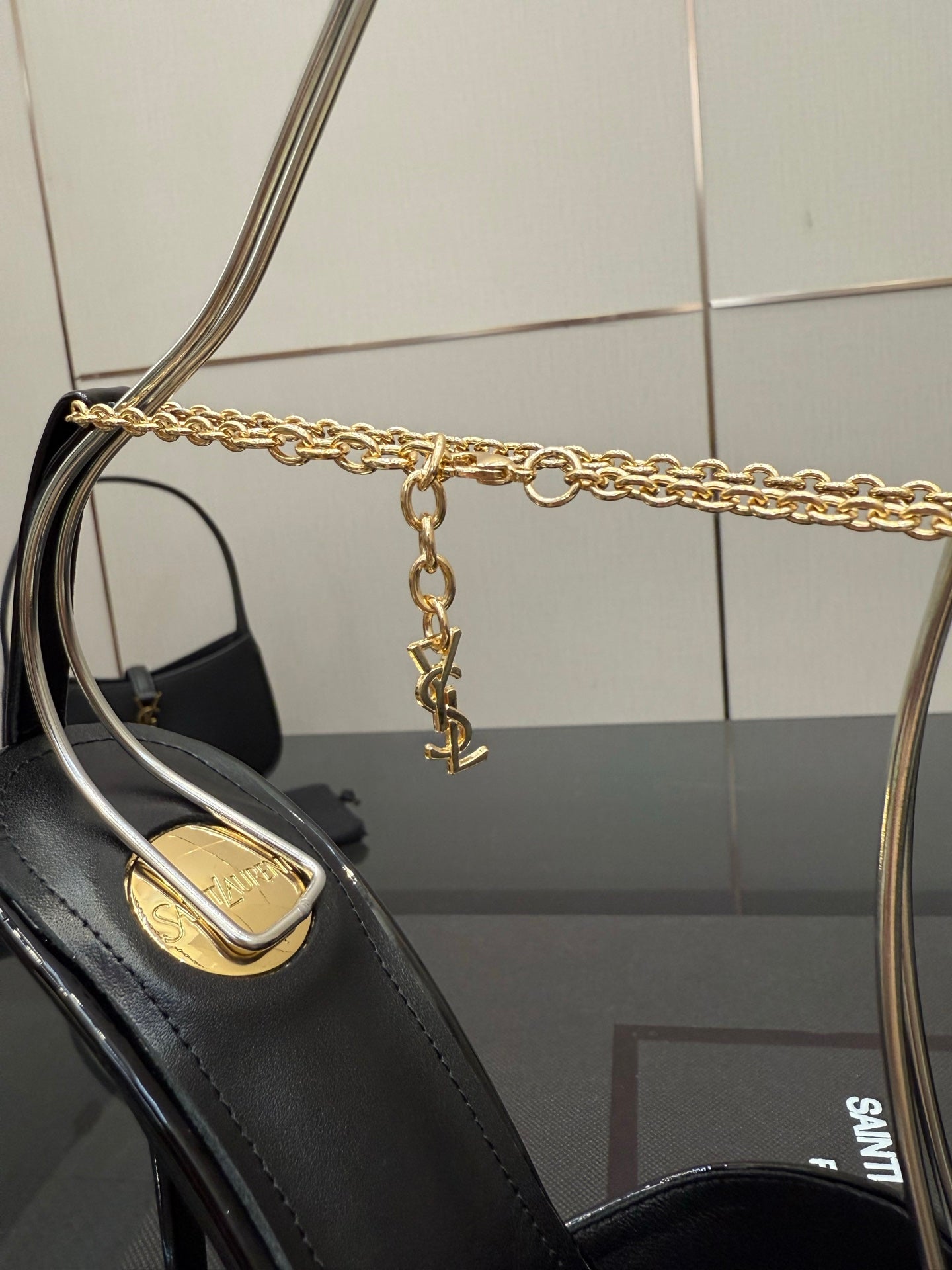 Black patent leather high-heel pump with gold chain strap and logo heel inlay