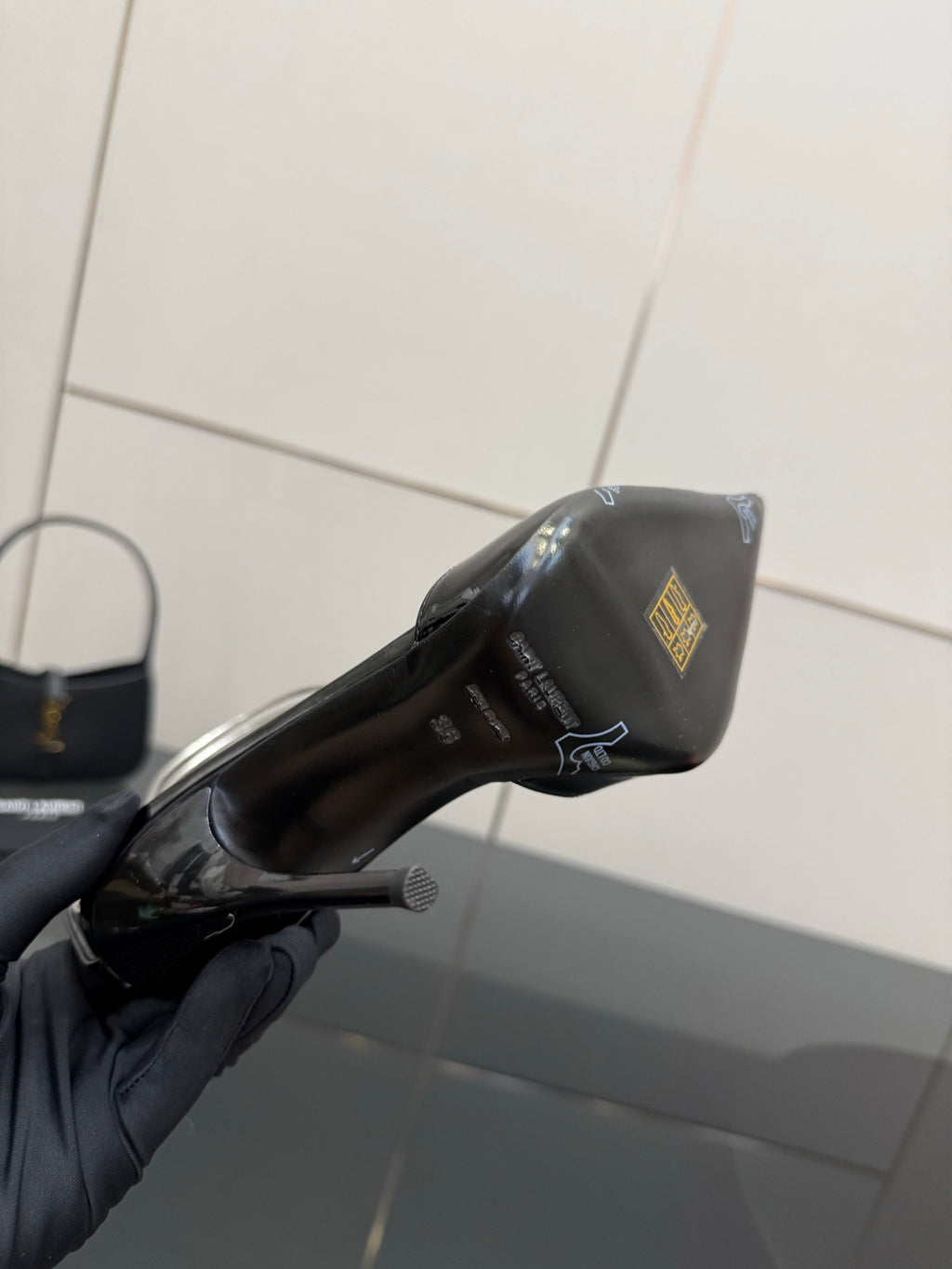 Black patent leather high-heel pump close-up with small gold emblem on side