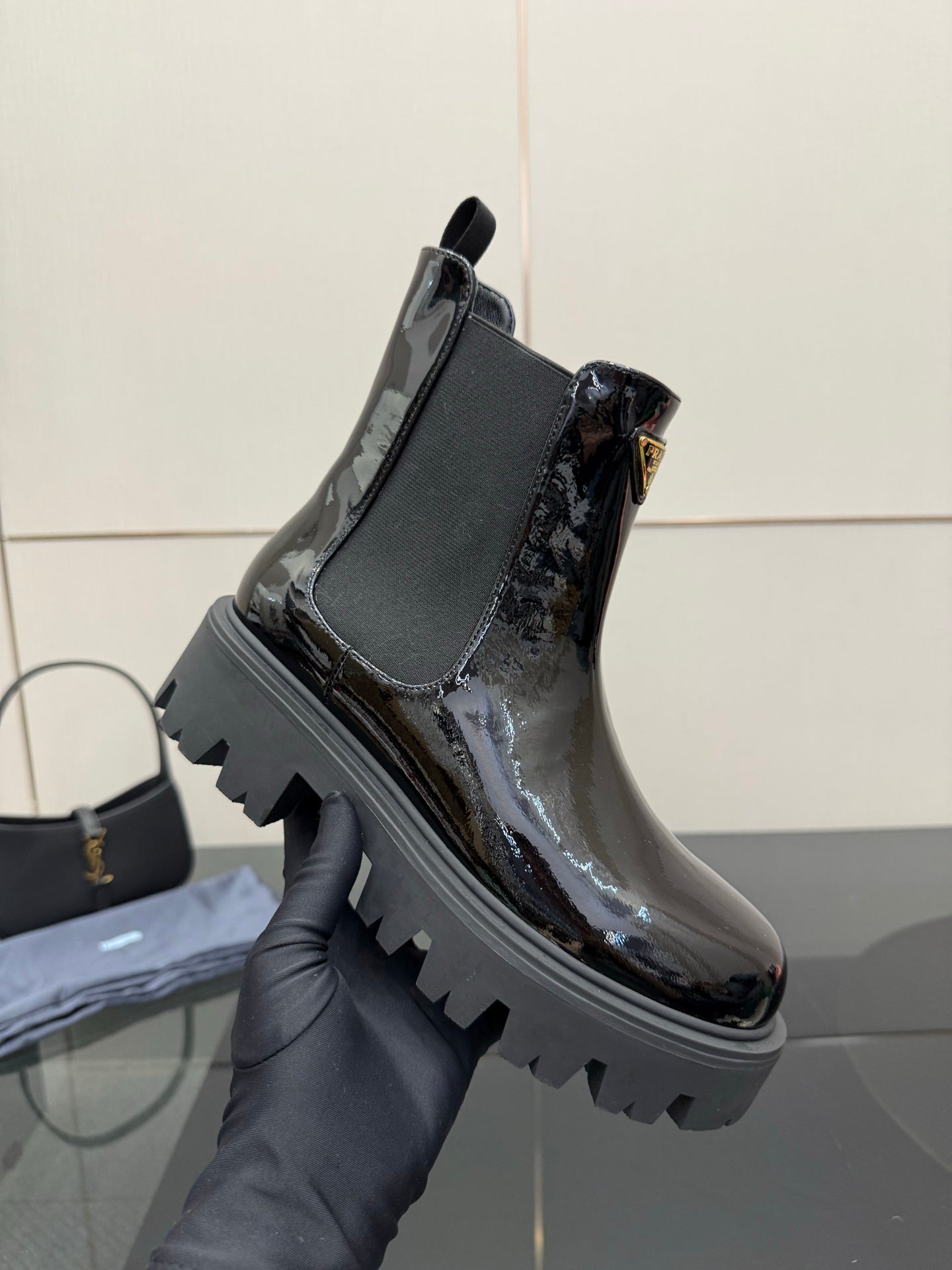 Black patent Chelsea boot on hand, thick lug sole and pull tab detail