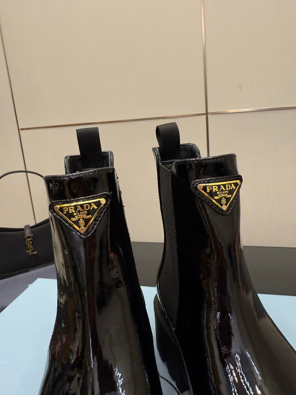 Black patent Chelsea boots close-up showing Prada logo badge on side