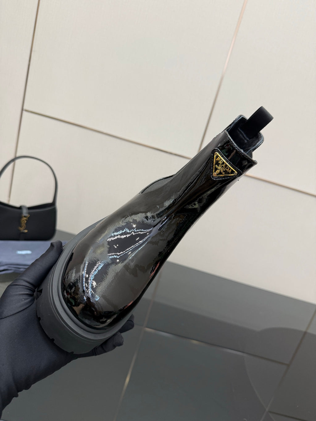 Black patent Chelsea boot held by hand, side Prada logo badge visible