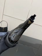 Black patent Chelsea boot held by hand, side Prada logo badge visible