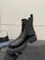Black patent Chelsea boot held by hand with chunky lug sole and pull tab