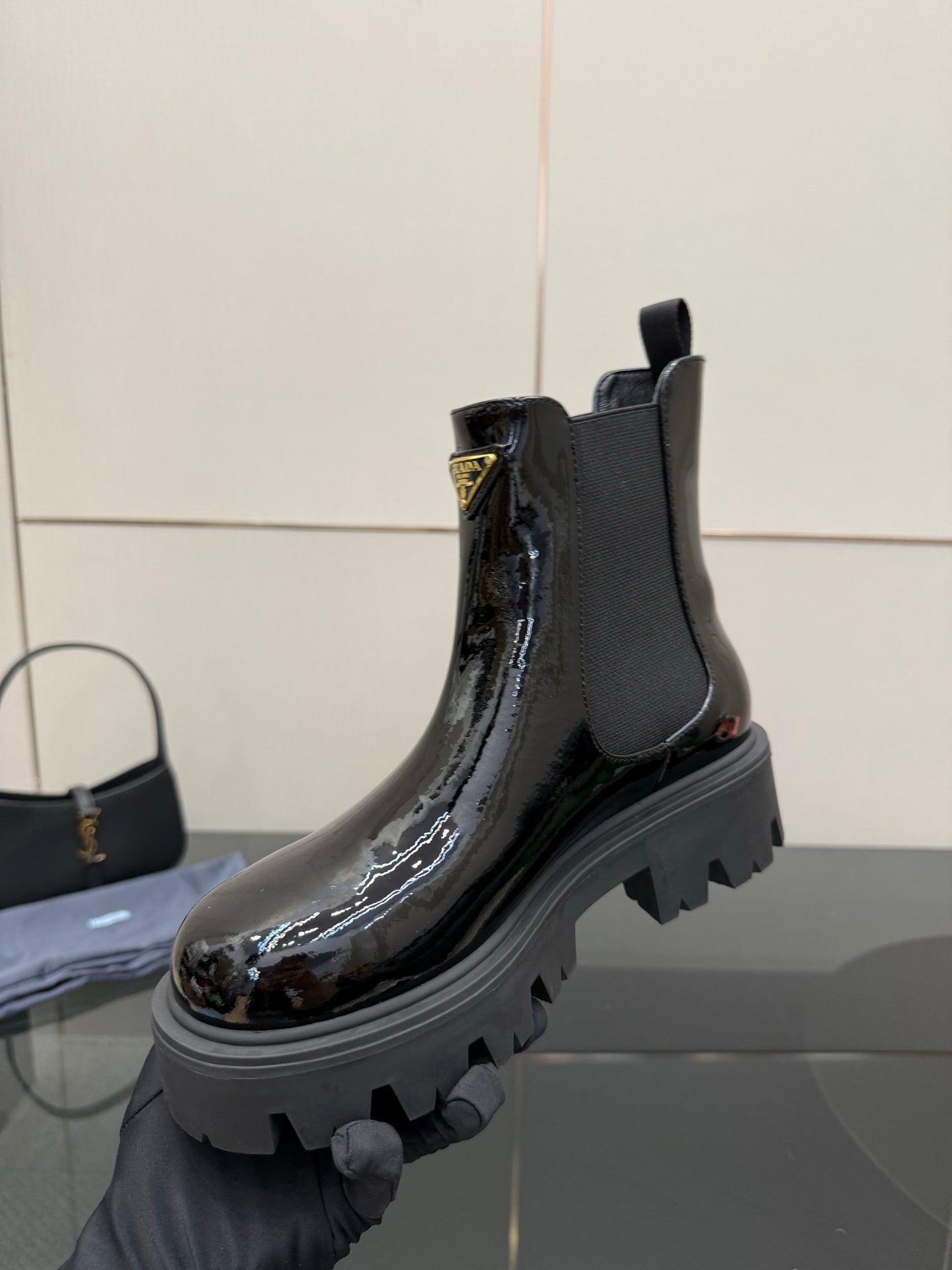 Black patent Chelsea boot held by hand with chunky lug sole and pull tab
