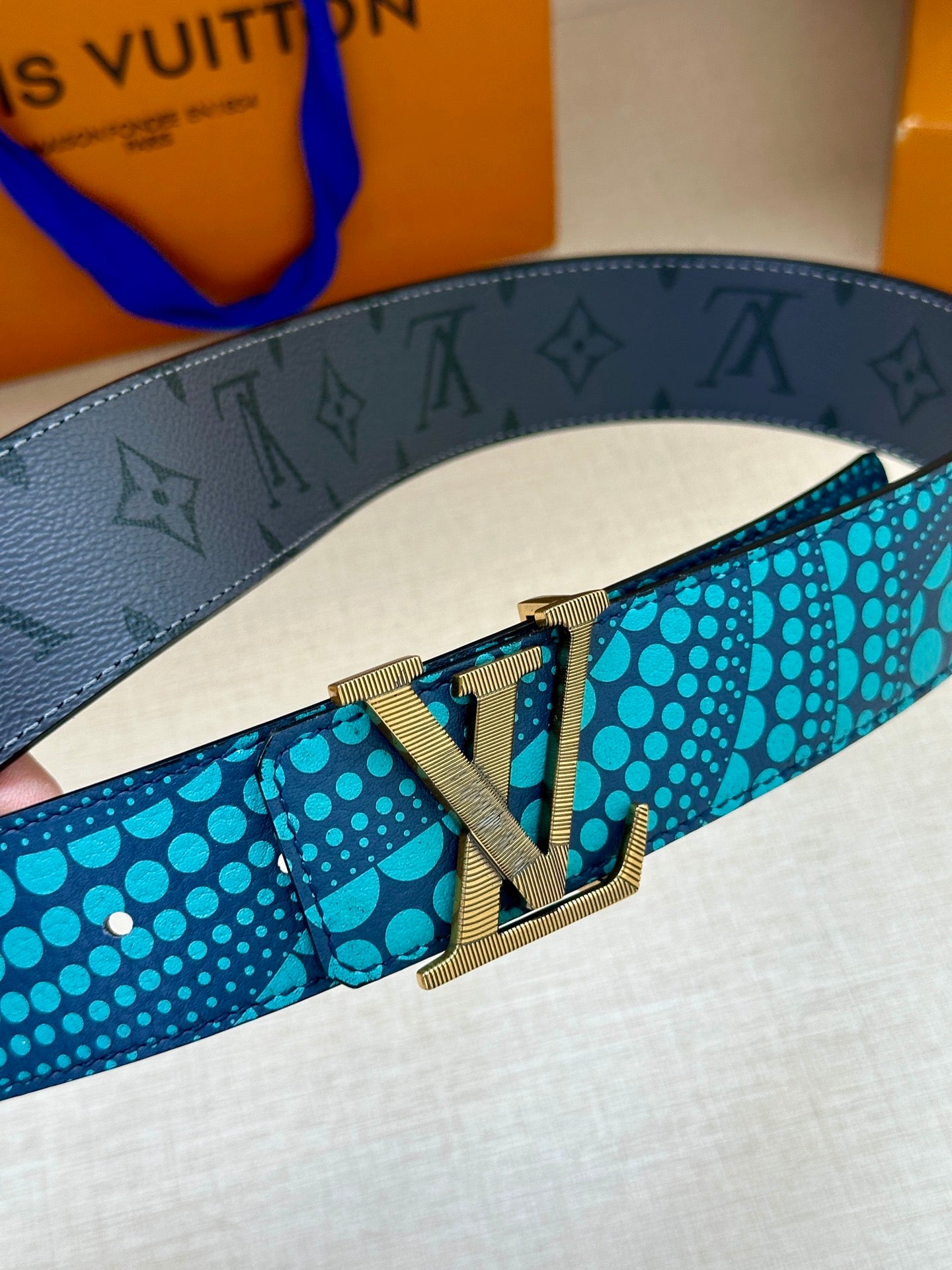 Louis Vuitton belt close-up: dark monogram strap, turquoise dots, gold buckle