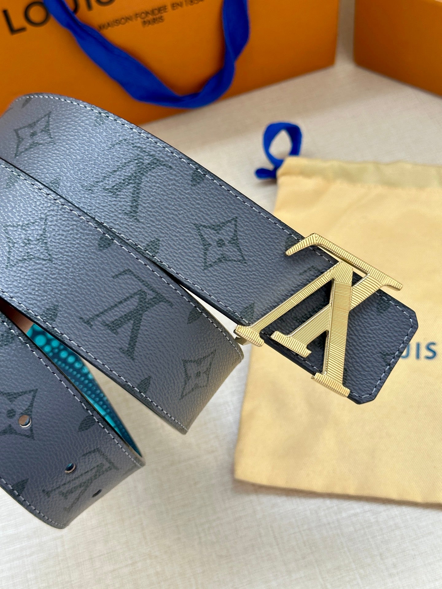 Louis Vuitton belt close-up: dark monogram strap, turquoise edge, gold LV buckle