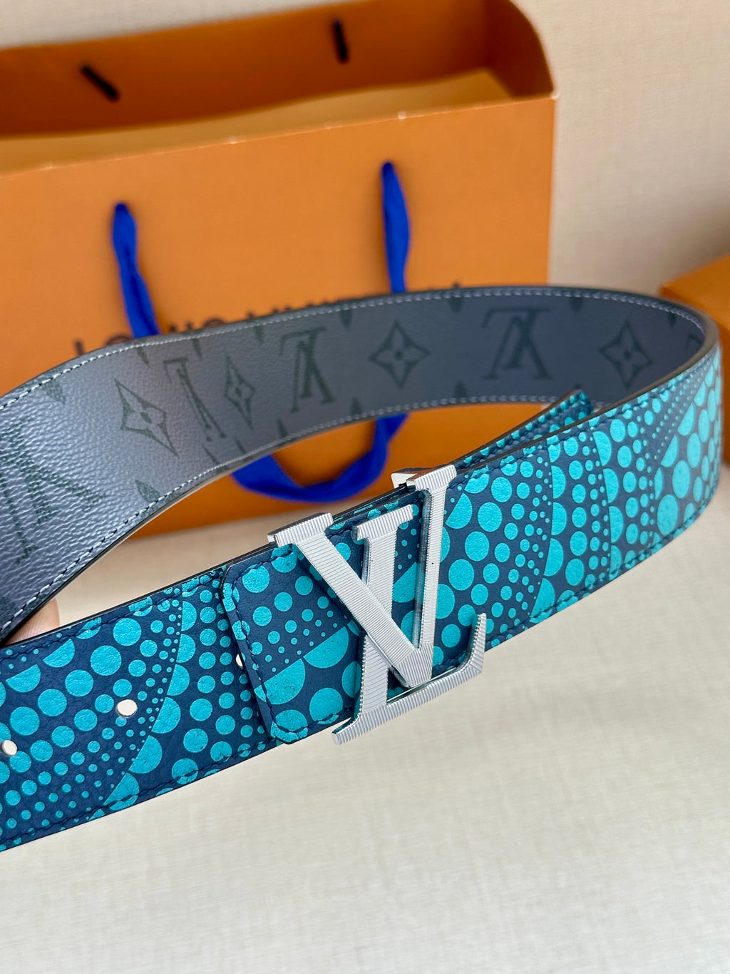 Louis Vuitton belt with turquoise dotted strap and silver LV buckle, angled view