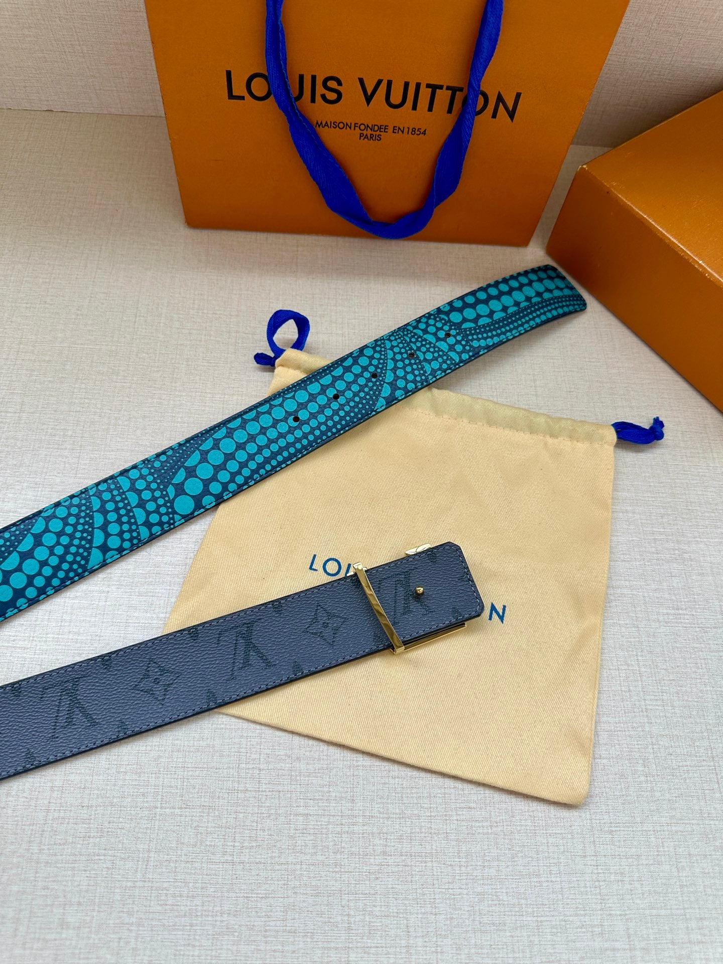 Louis Vuitton belt with turquoise dotted strap and dark monogram keeper, flat lay