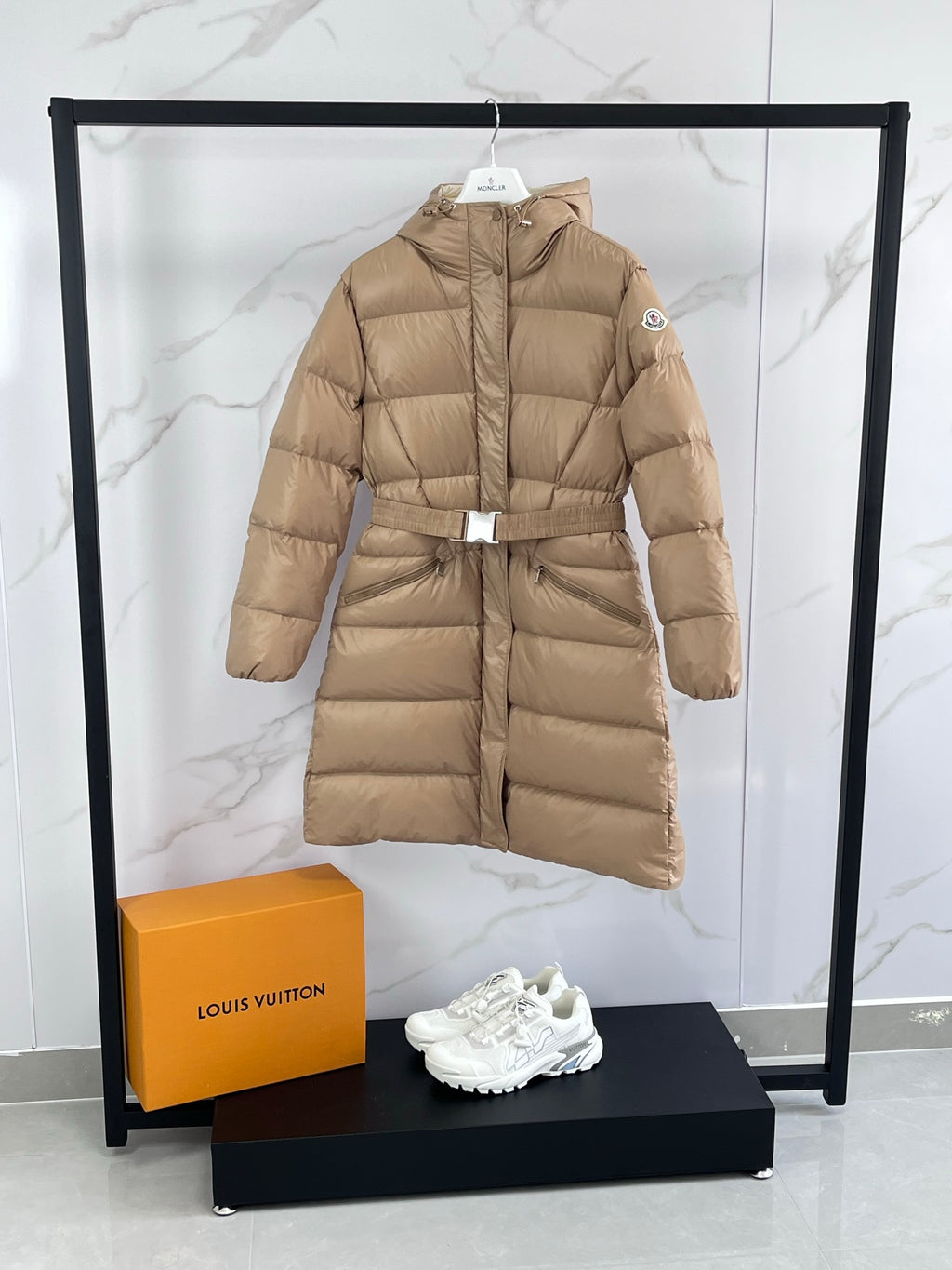 Tan long puffer coat with hood, front zip, and belt at waist